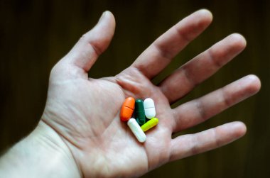 Açık erkek elinde iki beyaz, kırmızı, yeşil, sarı haplar var.