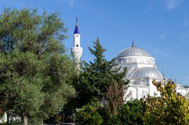 Yeşil yaprak ağaçları arasında tek minaresi olan ve Türkiye 'nin Cirali kentindeki mavi gökyüzüne karşı duran dev beyaz cami.