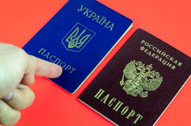 Kırmızı arka planda iki ulusal pasaport, kırmızı Rus pasaportu ve mavi Ukrayna pasaportu, işaret parmağı Ukrayna pasaportu.