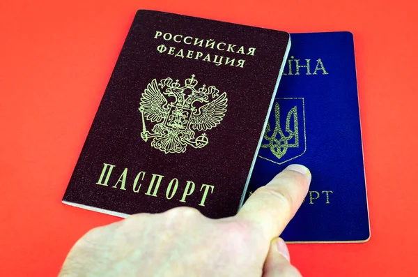 Two national internal passports lying on red background, red Russian passport and blue Ukrainian passport, index finger points to Ukrainian passport