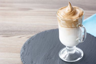 Dalgona Kahvesi, şeffaf, güzel bir bardakta buzlu, son moda Kore kremalı kremalı hazır kahveyi masa üzerinde mavi bir peçeteyle birlikte bir levhada. Boşluğu kopyala
