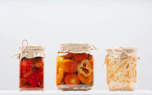 Várias verduras cultivadas fermentadas conservadas em escabeche em um jarro de vidro de enlatamento em uma mesa branca — Fotografia de Stock