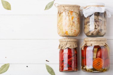 Fermente edilmiş sebze, lahana, domates, biber, havuç, mantar, beyaz masada konserve konservesi için cam bir kavanoza karıştır, köşelerde defne yaprakları, karabiber, kişniş. Üst Manzara. yatay.