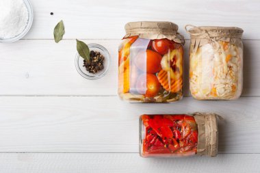 Turşulu mayalanmış lahana, domates, biber, havuç, çeşitli, cam kavanozda karıştırılmış beyaz ahşap masa, defne yaprağı, karabiber, kişniş tohumu, tuz. Üst Manzara. yatay.