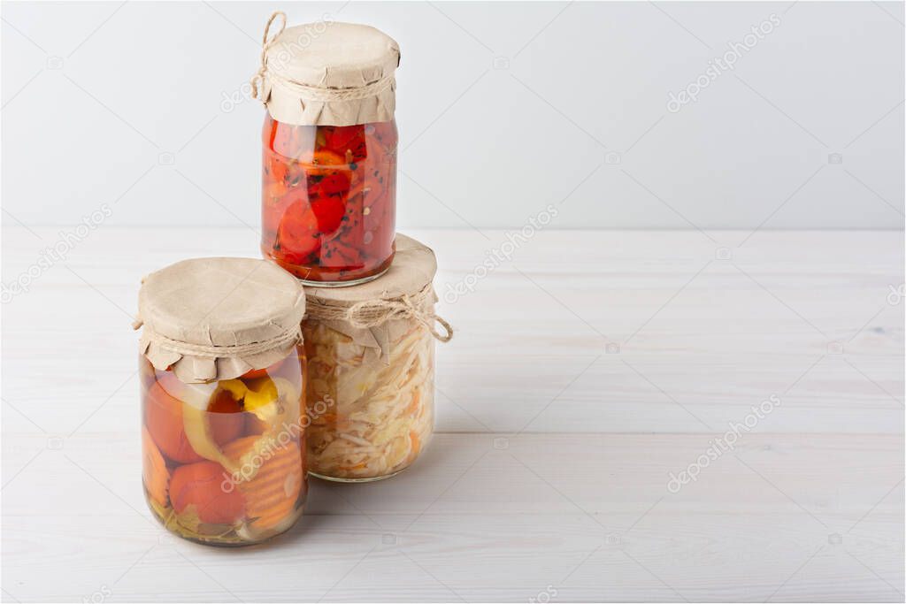 Pickled fermented cultivated cabbage, tomatoes, peppers, carrots, assorted, mix in a glass jar for canning on white wooden table. stand by the pyramid in the left corner. angle view. horizontal.
