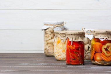 Turşulu mayalanmış lahana turşusu, domates, biber, havuç, mantar suillaceae kahverengi ahşap bir masa ve beyaz arka planda cam kavanozlarda çeşitli. yatay.