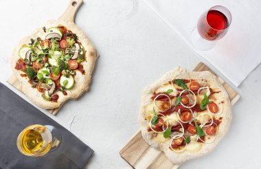 Brokoli, kabak, domates, mantar, mikroçerez, soğan, roka ve mozzarella ile birlikte iki çeşit vejetaryen pizza. Masanın üzerinde. Kırmızı ve beyaz şarapla. Üst görünüm.