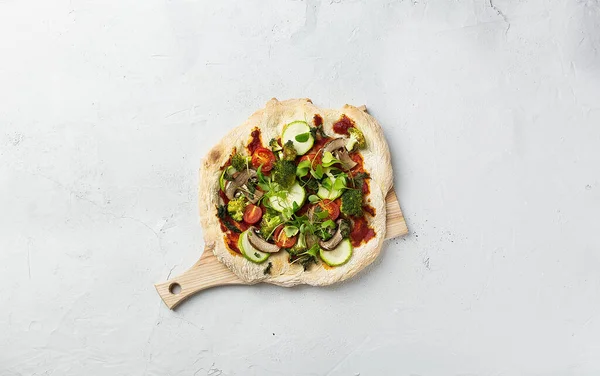 Vegetarian pinsa with vegetables on Roman pastry with broccoli, zucchini, tomatoes, mushrooms, microgreens. No cheese. on a wooden board and concrete background. Top view centrally located. Copy space