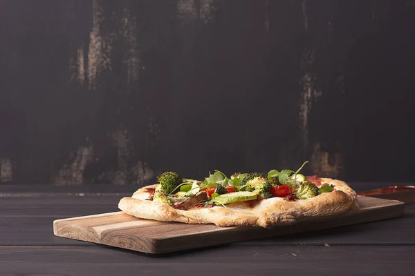 Vegetarian pinsa with vegetables on Roman pastry with broccoli, zucchini, tomatoes, mushrooms, microgreens. No cheese. Copy space. on a dark wooden background. rustic