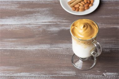 Dalgona Buzlu Kahve. Kahverengi ahşap arka planda, sütlü, çırpılmış, siyah bir Kore kahvesi. Bademlerle dolu beyaz bir tabakta. Uzayı kopyala Yan görünüm.