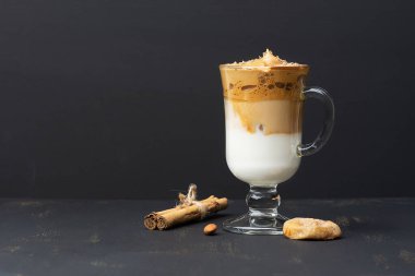 Dalgona Kahve Buzlu, koyu ahşap arka planda, sütlü, çırpılmış, siyah bir Kore kahvesi. Kurutulmuş incir, badem, tarçınlı çubuk, çikolata parçalı. Uzayı kopyala Yan görünüm.