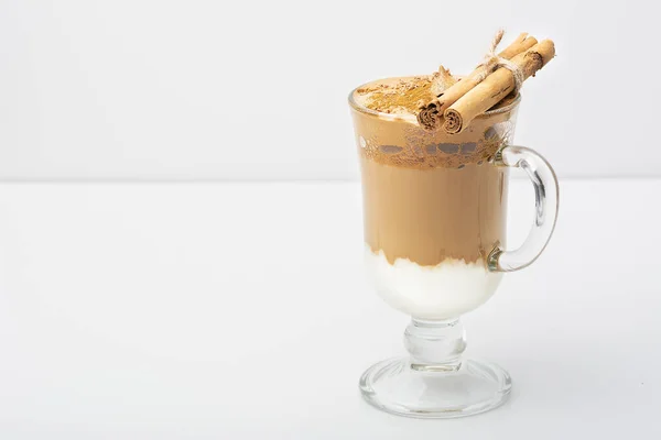 Dalgona Coffee Iced, a Korean fashionable whipped black instant coffee with milk, on a white background. On a glass of cinnamon sticks and chocolate chips. Copy space. Direct view.