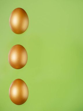 Açık yeşil arka planda yatan üç altın yumurtadan oluşan dikey sıra. İzole edilmiş altın boyalı tavuk yumurtaları. Paskalya kavramsal tatil illüstrasyonu