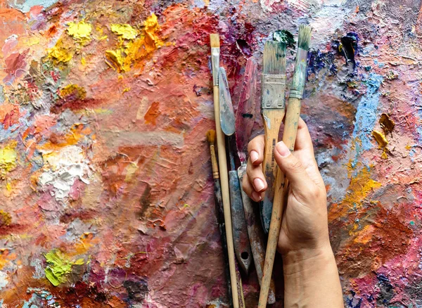 Artist\'s hand with brushes for painting on a palette stained with bright colors