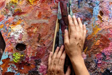 Parlak renklerle boyanmış bir paleti boyamak için fırçalı sanatçının elleri