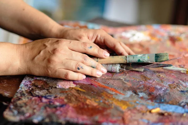 Artist\'s hands with brushes for painting on a palette stained with bright colors
