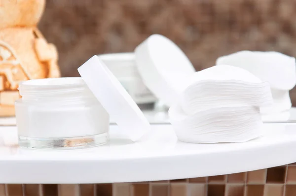 Kahverengi aroma lambası, yanan bir mum, pamuk pedler ve krema banyoda beyaz bir rafta. Yüz ve vücut derisi için kişisel bakım. Banyodaki yapbozlu ayna ve raf..