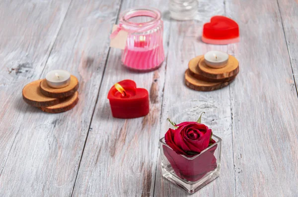 Pink scented candle in a glass jar, small candles on wooden coasters, a burning heart candle and a small decorative soap heart on a gray wooden table. Valentine\'s Day. Greeting card. The background.