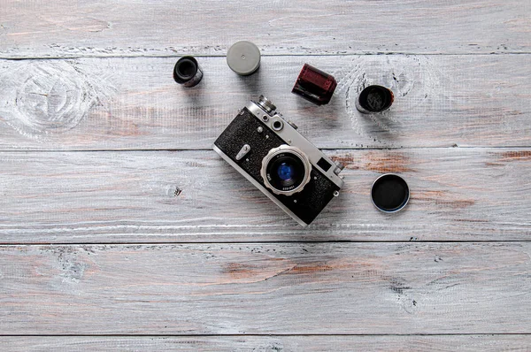 Old camera, bag and films on a gray wooden table. A vintage camera stands on a table with photographic films.