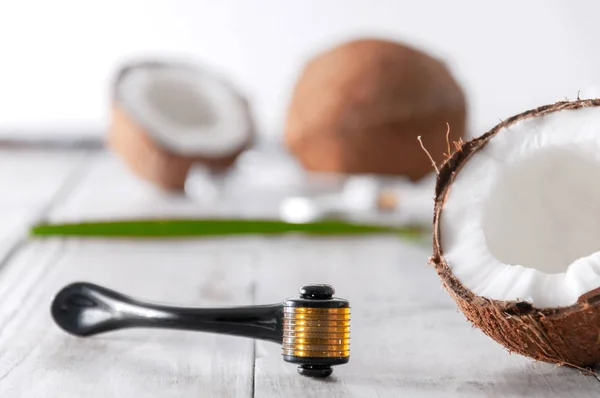 Yarısı hindistan cevizi, cam şişede gerekli yağ, krem ve yüz masajı aleti gri ahşap bir masada. Kişisel bakım. Spa tedavileri. Kozmetoloji. Doğal ve organik kozmetik ürünler.