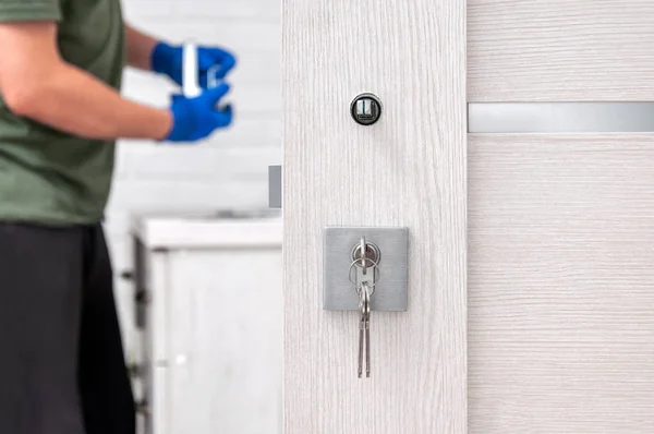 Adam yeni kapı kolları takıyor ve odanın kapısını kilitliyor. Evde tamirat var. Mavi eldivenli adam kapı kollarını tutuyor. Kapı kilidi takılıyor.