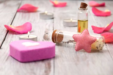 Temel yağlar, kalp şeklinde pembe tuz banyosu bombası, gri ahşap bir masada gül yaprakları. Yüz ve vücut bakımı. Spa tedavileri.
