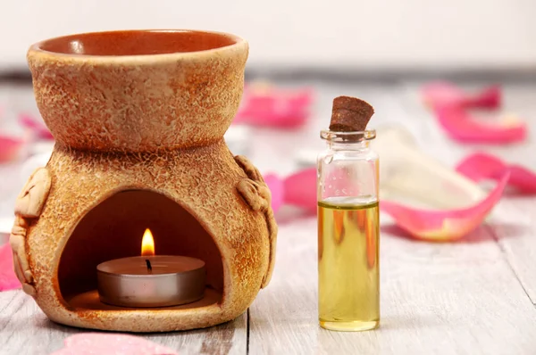 Aroma lambası yanan bir mum ve gerekli yağlar, kalp şeklinde pembe tuz banyosu bombası, gri ahşap bir masada gül yaprakları. Yüz ve vücut bakımı. Spa tedavileri.