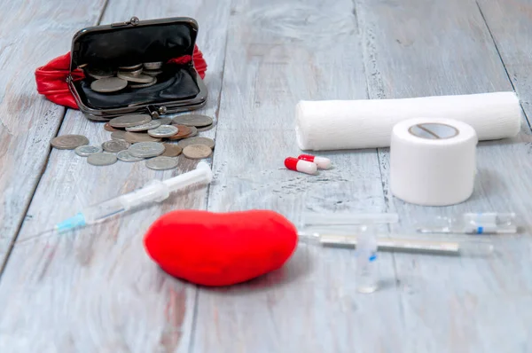 Wallet with coins, heart and medicine on a gray wooden table. Health care. Ambulance. First Aid Kit. Healthcare and medicine.