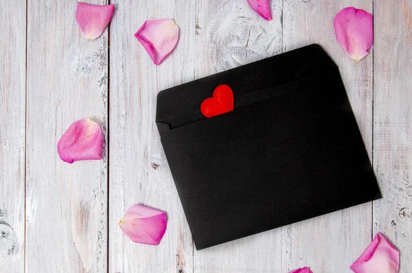 Rotes Herz Auf Schwarzem Umschlag Und Rosenblätter Auf Grauem Holzgrund — Stockfoto