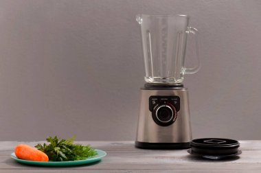 Blender, havuç, maydanoz, gri ahşap bir masada dereotu. Kız sebze püresi yapıyor. Sağlıklı bir yaşam tarzı. Beslenme düzeni. Havuç ve yeşillik yakın plan..