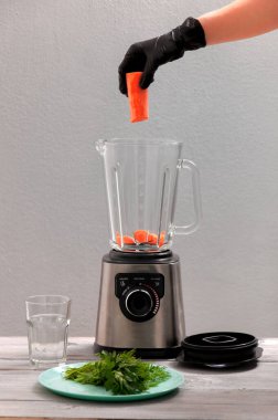 Blender, havuç, maydanoz, gri ahşap bir masada dereotu. Kız sebze püresi yapıyor. Sağlıklı bir yaşam tarzı. Beslenme düzeni. Havuç ve yeşillik yakın plan..