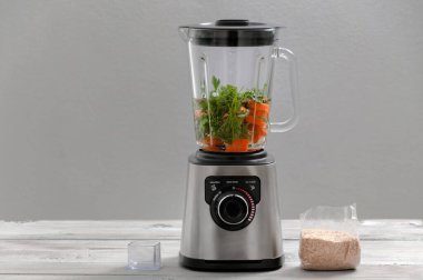 Blender, havuç, maydanoz, gri ahşap bir masada dereotu. Kız sebze püresi yapıyor. Sağlıklı bir yaşam tarzı. Beslenme düzeni. Havuç ve yeşillik yakın plan..