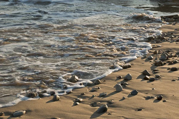 Vagues se lavant sur de petits rochers et galets sur une plage — Photo
