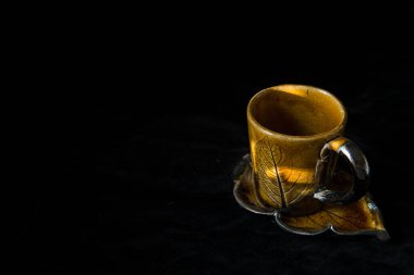 Bir turuncu el kahve fincanı, siyah arka planda fincan tabağı, güneş ışığı ve metin için yer.