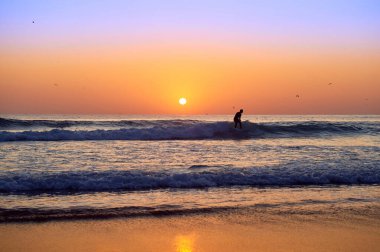 Adam gün batımında Portekiz 'de Atlantik Okyanusu' nda tek başına sörf yapıyor.