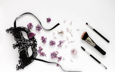 Maskeli balo maskesi, bahar çiçekleri ve beyaz arka planda püsküller. Mor çiçekler rastgele dağılmış.