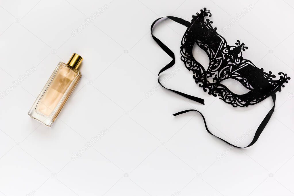 Carnival black mask and perfume bottle in gold color on a white background.