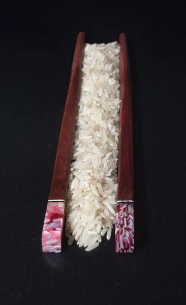 Tahta yemek çubukları ve koyu arkaplanda biraz basmati pilavı..