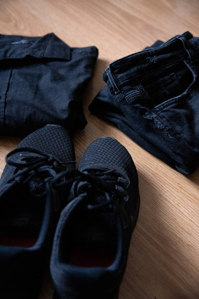 Натюрморты черные кроссовки, сложенная черная рубашка и черные брюки на деревянном фоне. Вертикальное изображение
.