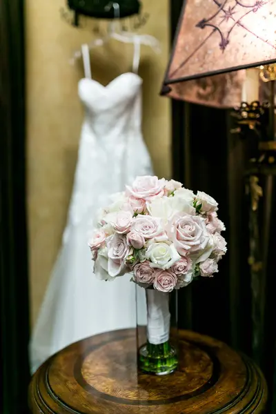 rose wedding bouquet with white wedding dress in background