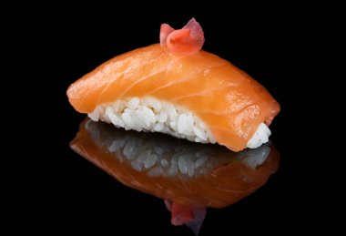 Siyah ayna yüzeyinde suşi nigiri. Tabak bir dilim zencefil turşusuyla süslenmiş..