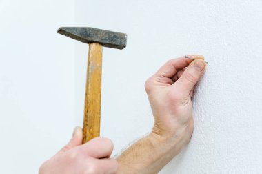 Bir adamın eli duvara çivi çakıyor..
