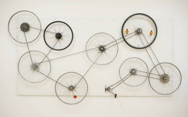 Duvarda bisiklet tekerlekleri, kişisel sanat ihtirası, galeri, pedal, konserve. Tekerlekler birbirine bağlıdır ve pedalı çevirerek tüm çarklar hareket eder. Evrendeki her şeyin birbirine bağlılığını temsil eder..