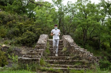 Mavi maskeli genç ormanda bir köprüde merdivenlerden iniyor..