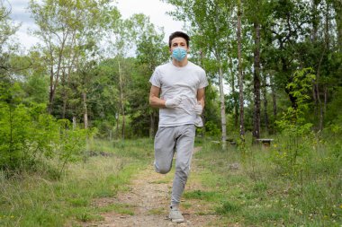 Ormanda koşan mavi maskeli ve beyaz eldivenli genç bir çocuk..