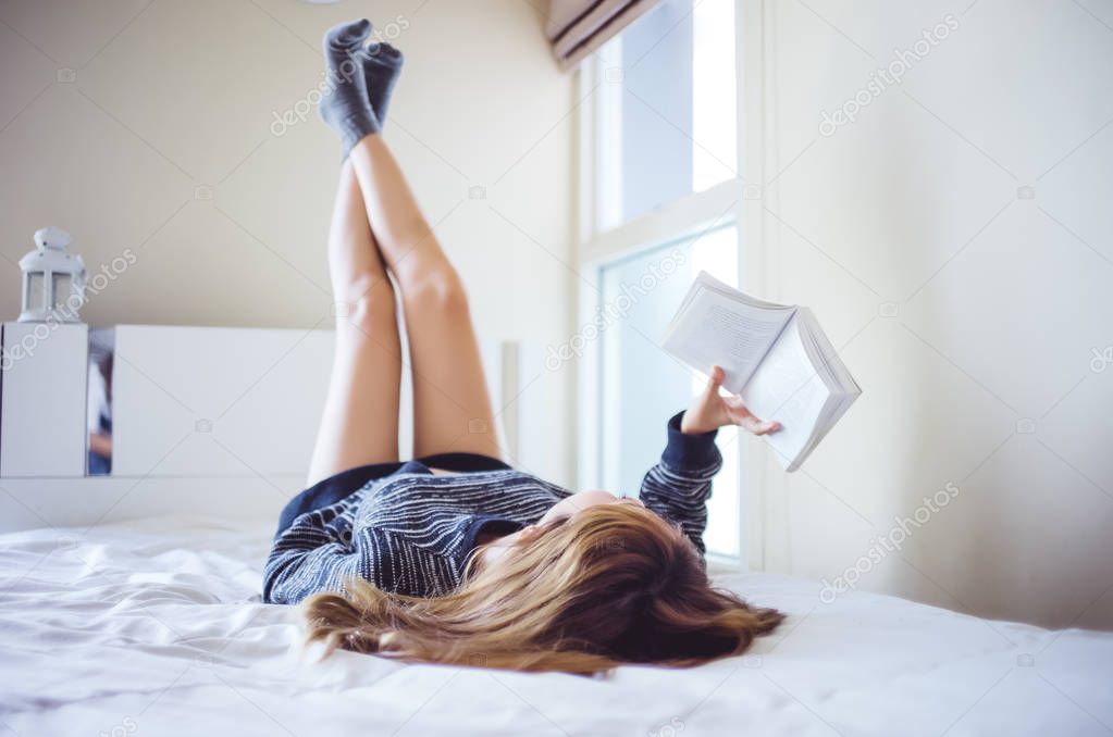 Young happy woman lying on bed  and reading a book, lifting his 