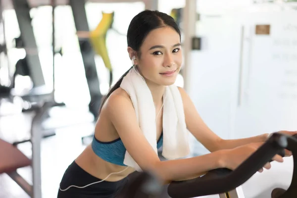 Musculosa joven sonriendo haciendo ejercicio en la bicicleta estática en —  Fotos de Stock