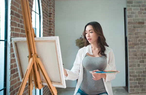 Beautiful young woman painting on a canvas in art studio — Stock Photo, Image