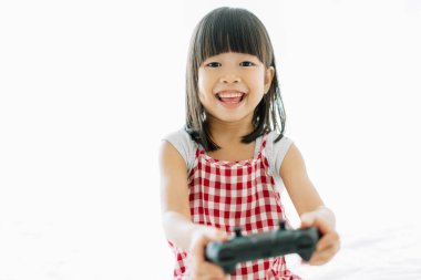 Mutlu çocuk, küçük Asyalı bir kız yatakta oturmuş video oynuyor. 