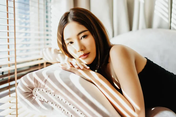 Portrét sexy mladé asijské ženy v černých šatech ležící na pohovce — Stock fotografie